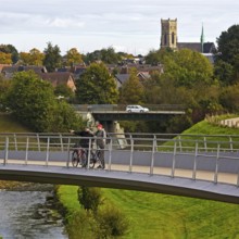 People on the bridge jump over the Emscher with the river below and St Lambert's Church in