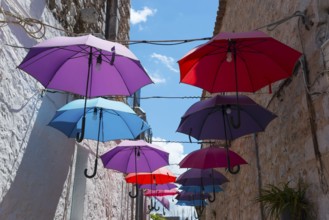 Colourful umbrellas hanging between old buildings under a clear blue sky, Old Town, Areopoli,