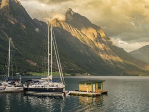 Boats and floating sauna, marina of village Urke at the Hjørundfjord, Mt. Slogen in the back,