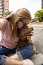 A affectionate woman hugs her pet, gives her dog a kiss on the forehead, and takes a photo