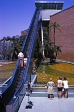 Menschen auf einer Rolltreppe im Freien, die über Wasserbecken und Palmen führt, USA, 1969,