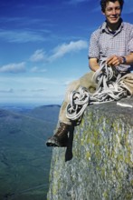 Young male climber sitting high up on a rock and holding a climbing rope, probably North Wales,