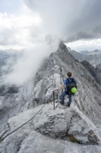 Mountaineer on a narrow rocky ridge on a steel cable, Watzmann crossing to Watzmann Mittelspitze,