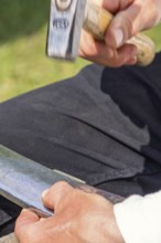 Man Peening a scythe blade using a hammer