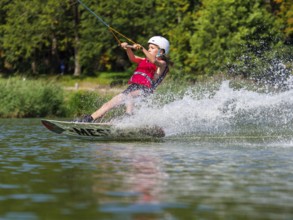 Boy or girl, water sports with wakeboard, red life jacket, water skiing in the wake park