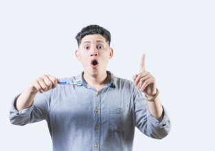 Surprised young man holding toothbrush pointing up isolated. Amazed man with toothbrush pointing up