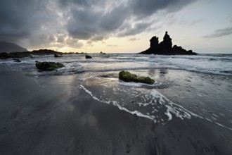 Dramatic cloudy atmosphere with rock formation at rising tide at sunset on the beach of Playa de