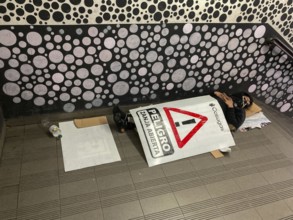 Homeless man sleeping in the entrance of the underground covered with a warning sign reading