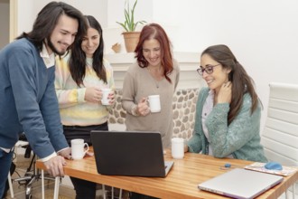 Smiling business professionals collaborate at a desk with a laptop in a creative office. They