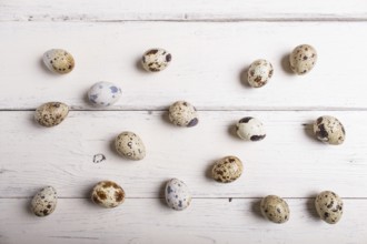 Raw quail eggs on a white wooden background, top view