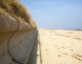 Wave return wall coastal defence and wide sandy beach submerging wooden groyne, Horsey, Norfolk,