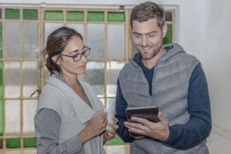 Two colleagues discuss their work looking at a tablet, with friendly expressions and concentrated.