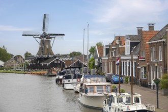 Dutch scenery with windmill, boats and traditional houses along a water canal, Woudsend, province