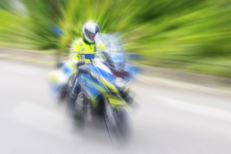 Policeman on a motorbike driving fast along the road, the speed is emphasised by the motion blur,