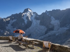 Mountain hut Cabane de l'A Neuve, tourists sitting on terrace, Aiguille Rouges du Dolent massif at