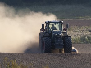 Agricultural tractor, cultivating a field, after the corn harvest, surrounded by dust due to very