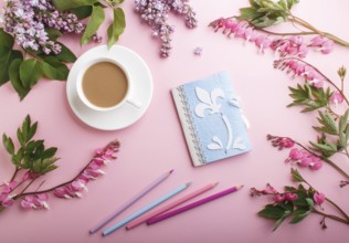 Purple lilac flowers and a cup of coffee with notebook and colored pencils on pastel pink