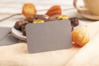 Gray business card with chocolate candies and physalis flowers on a white wooden background and