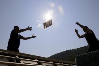 Silhouettes of two roofers throwing tiles at each other against the light