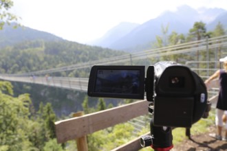 Close-up of a camcorder during video recording in nature. The mountains (Alps) and tourists can be