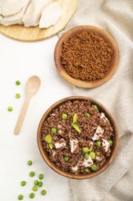 Quinoa porridge with green pea and chicken in wooden bowl on a white wooden background and linen