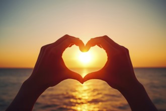 Two hands forming a heart shape, silhouetted against a breathtaking ocean sunset. Love and warmth