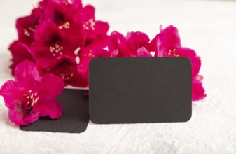 Black business card with purple azalea flowers on gray concrete background. side view, copy space,