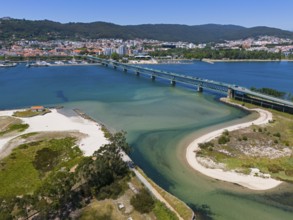 View of a city on the water with a large bridge crossing an estuary, surrounded by mountains and