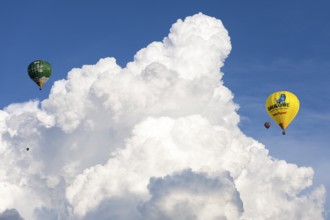 Two hot air balloons flying in front of big white clouds in the blue sky, Baden-Württemberg,