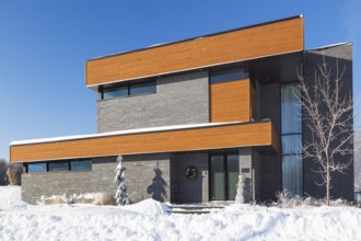 Modern grey brick and stained wood finish cube style house facade with black trim in winter,