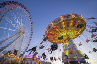 A funfair at dusk with illuminated chain carousel and Ferris wheel, Europa Rad, rides, wave flight,