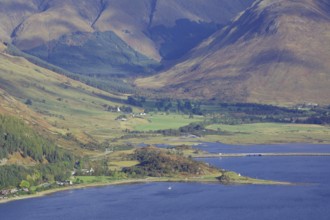 Green valley with a body of water and surrounded by high mountains under a blue sky, October,