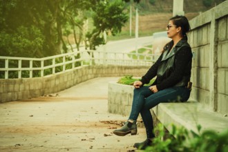 Attractive young woman with glasses sitting on a bench meditating. Relaxed girl sitting on a bench