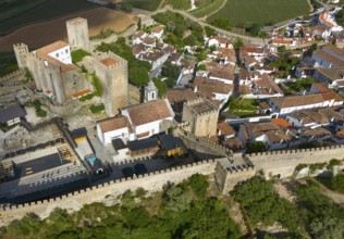 Aerial view of a historic city with a castle and surrounding city walls, embedded in a hilly and