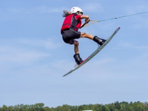 Boy or girl jumping with wakeboard, red life jacket, water sports, water skiing in wakepark