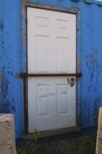 Blue painted metal building with white entrance door protected with steel bar, Quebec, Canada,