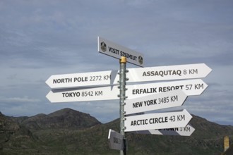 A signpost shows distances to various important places in front of a mountain landscape, Sisimuit,