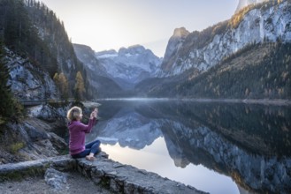 A woman doing yoga (Gomukhasana, Garudasana) by the lake. Vorderer Gosausee in autumn with a view