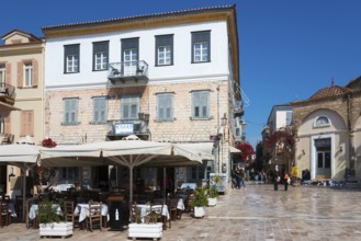 A square with a historic building, café with parasols and Mediterranean flair under a blue sky,