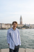 Young man in striped shirt and shorts on the banks of the Grand Canal, looking into the camera,