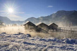 Boat huts in the morning light in front of mountains, lake, snow, sunbeams, winter, fog, Lake