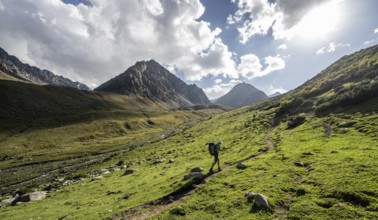 Mountaineers on a hiking trail, green high valley with mountain stream, Keldike Valley on the way