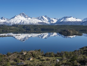 The snow-covered Mt. Cerro Castillo is reflected in a lake, small farm by the lake, Patagonia,