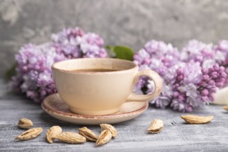 Cup of coffee with lilac and almonds on a gray wooden background. Side view, close up