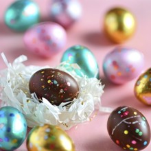 Small chocolate Easter eggs wrapped in shiny foil, placed on a bed of shredded pastel-colored