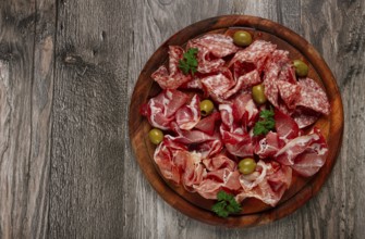 Assortment, sliced meat appetizer, prosciutto, salami and ham, with olives, on a wooden board,