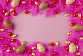 Frame made of eggs on pink feathers with red and gold chocolate eggs on a pink background