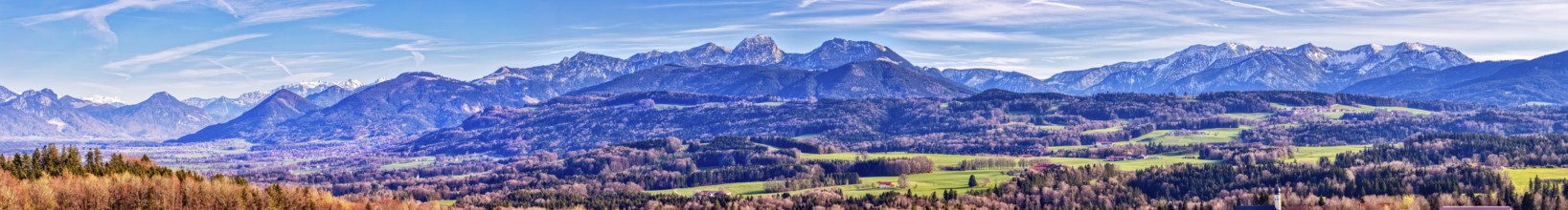 Expansive mountain landscape under a clear blue sky with few clouds and green fields, Irschenberg