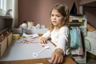 Girl playing creatively at a table in the children's room in front of a window, dreamy look