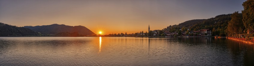 A peaceful sunset over a lake with mountains and a village in the background, Schliersee